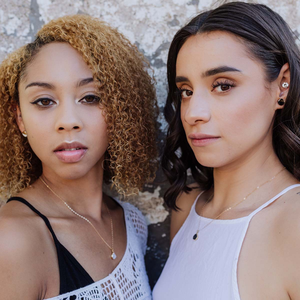 Two women wearing casual white clothing modeling crystal jewelry.