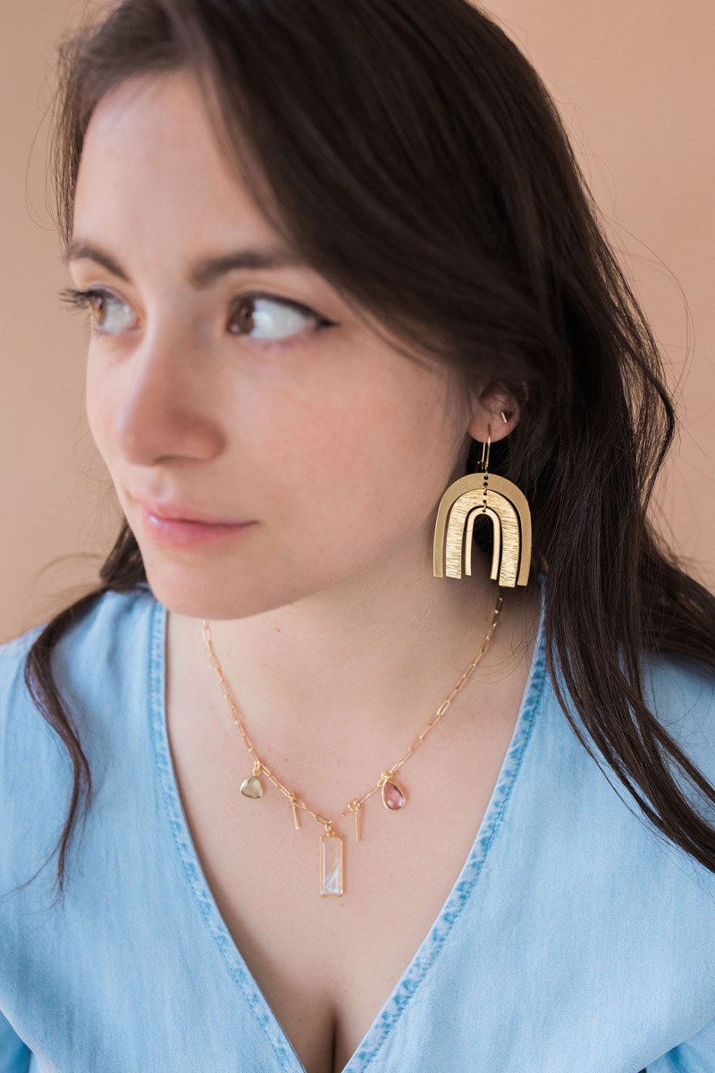 Woman wearing a blue blouse and modeling the Alectrona Earrings and Athena Necklace