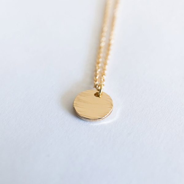 A close-up product photo of the Goddess of the Crossroads Necklace, a small round charm, gold-tone and lightly textured.