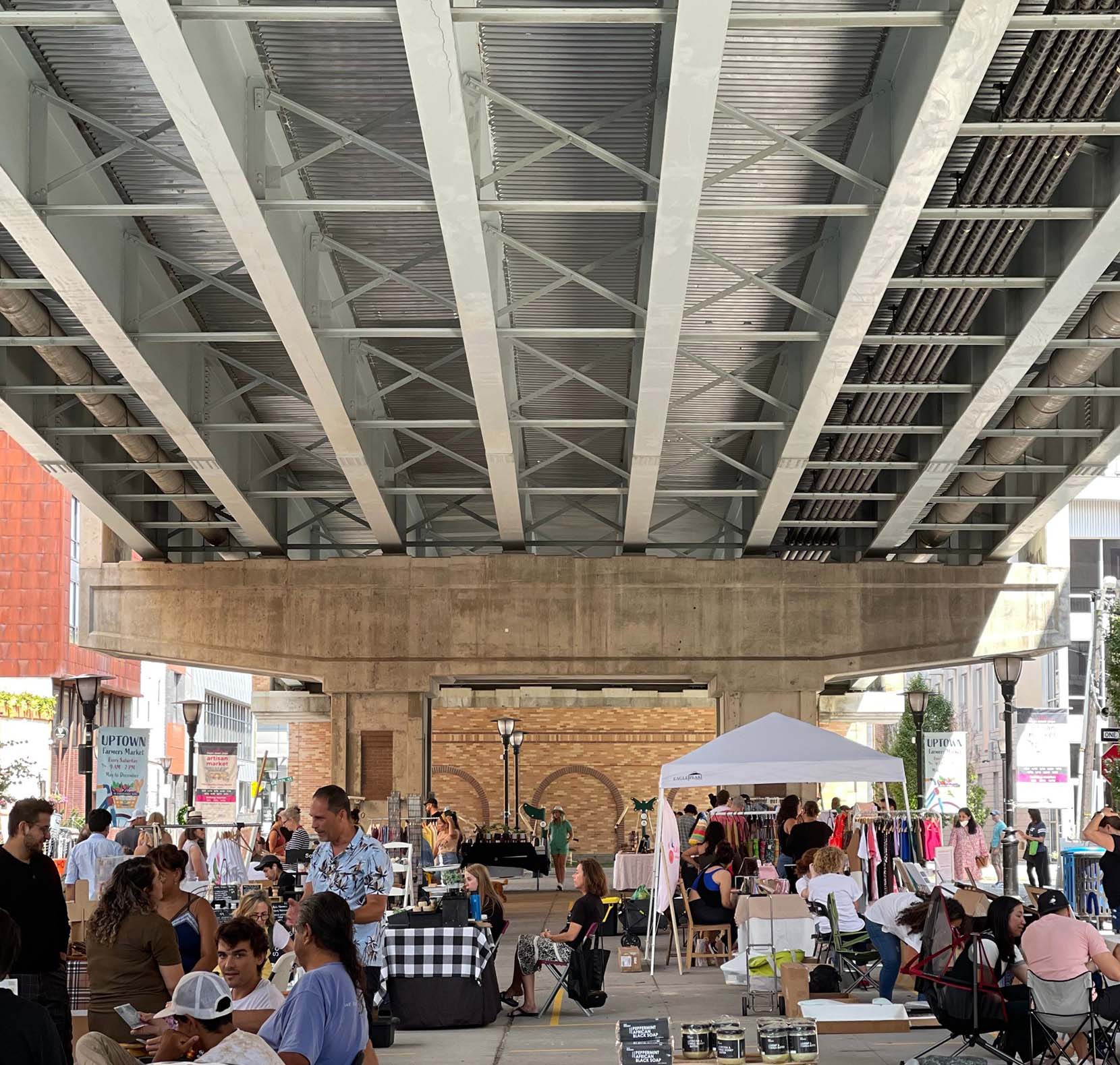 A crowded outdoor artisan market beneath a viaduct