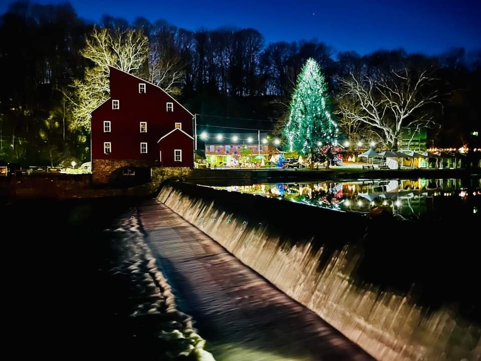 The Red Mill Museum seen from across a river, decorated with holiday lights