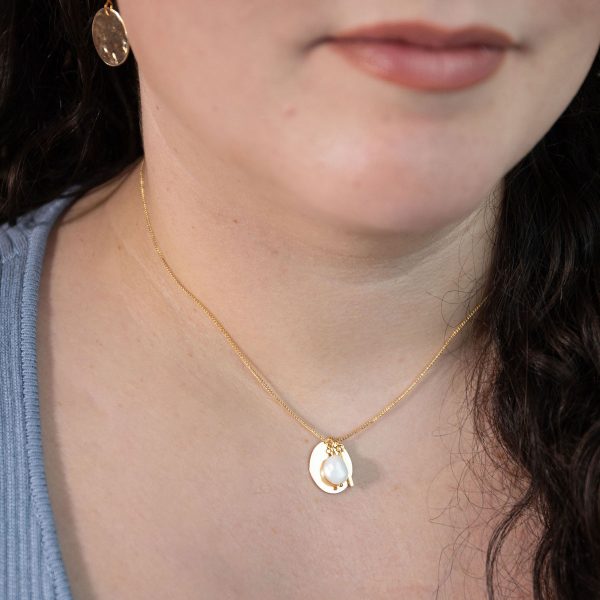 Closeup of a woman's neck modeling the Lady of the Empyrean Necklace, a white baroque pearl and tiny gold stick charm over a hammered oval pendant, strung on a dainty curb chain.