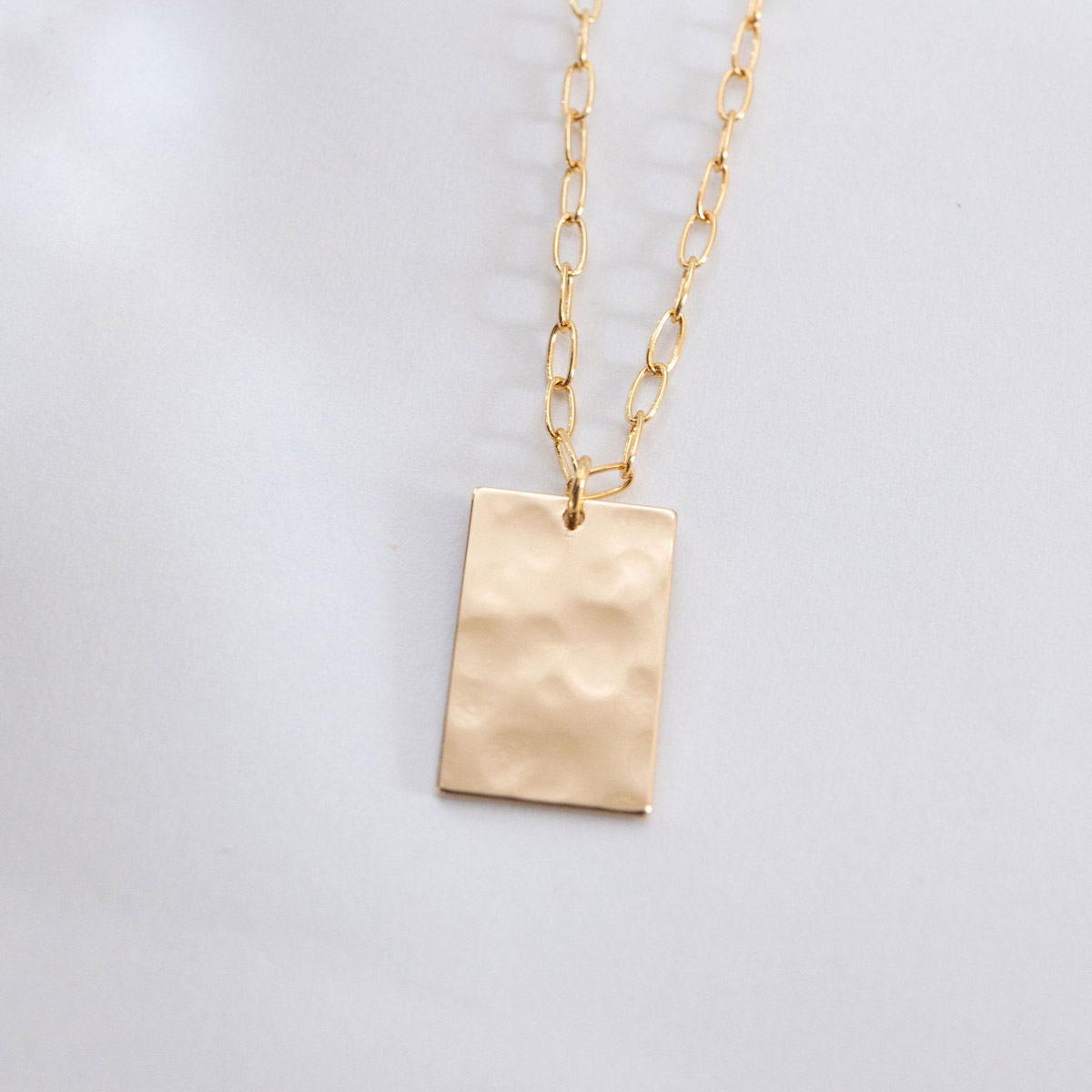 Zenith Necklace, a gold tone hammered ractangle charm on a dainty gold paperclip style chain.