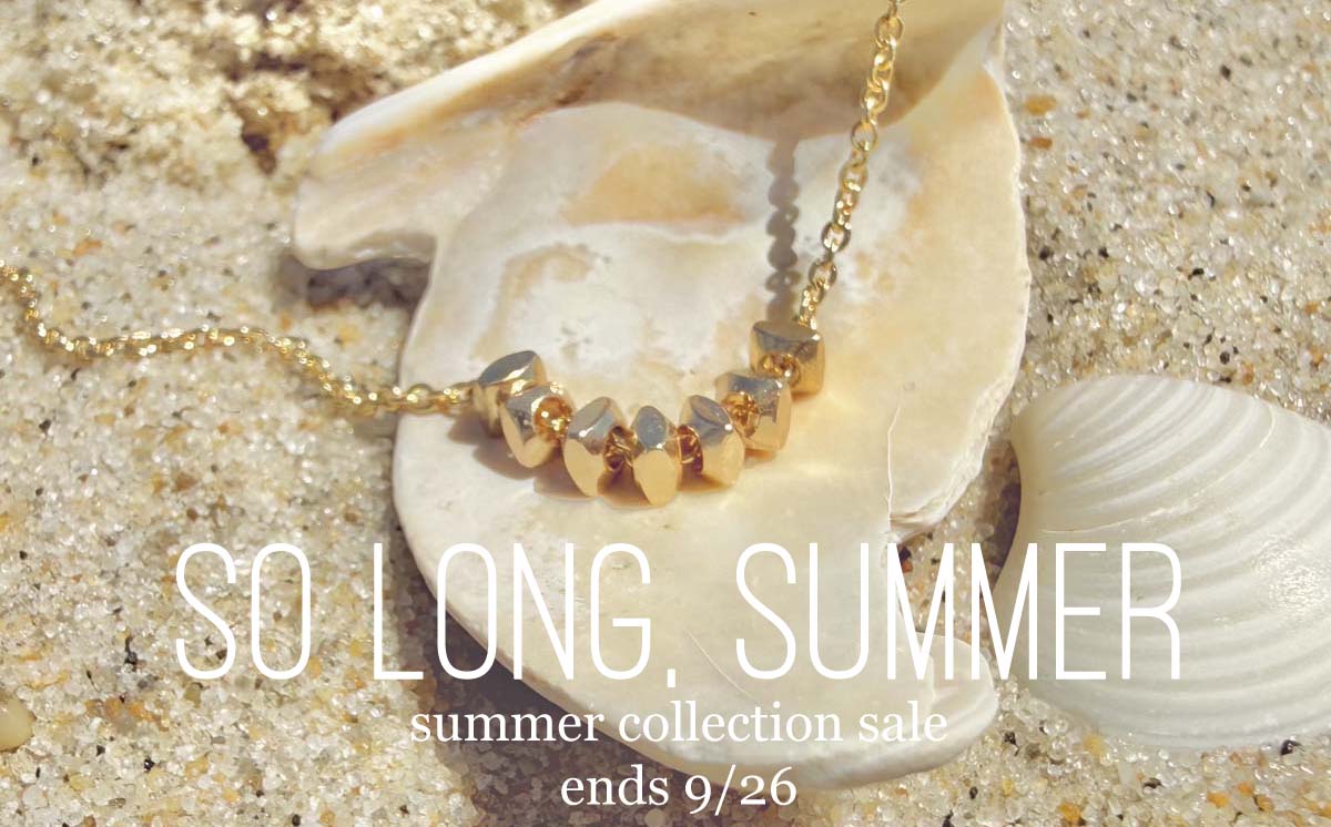 A beaded Crest of the Goddess Necklace display on a seashell in sand