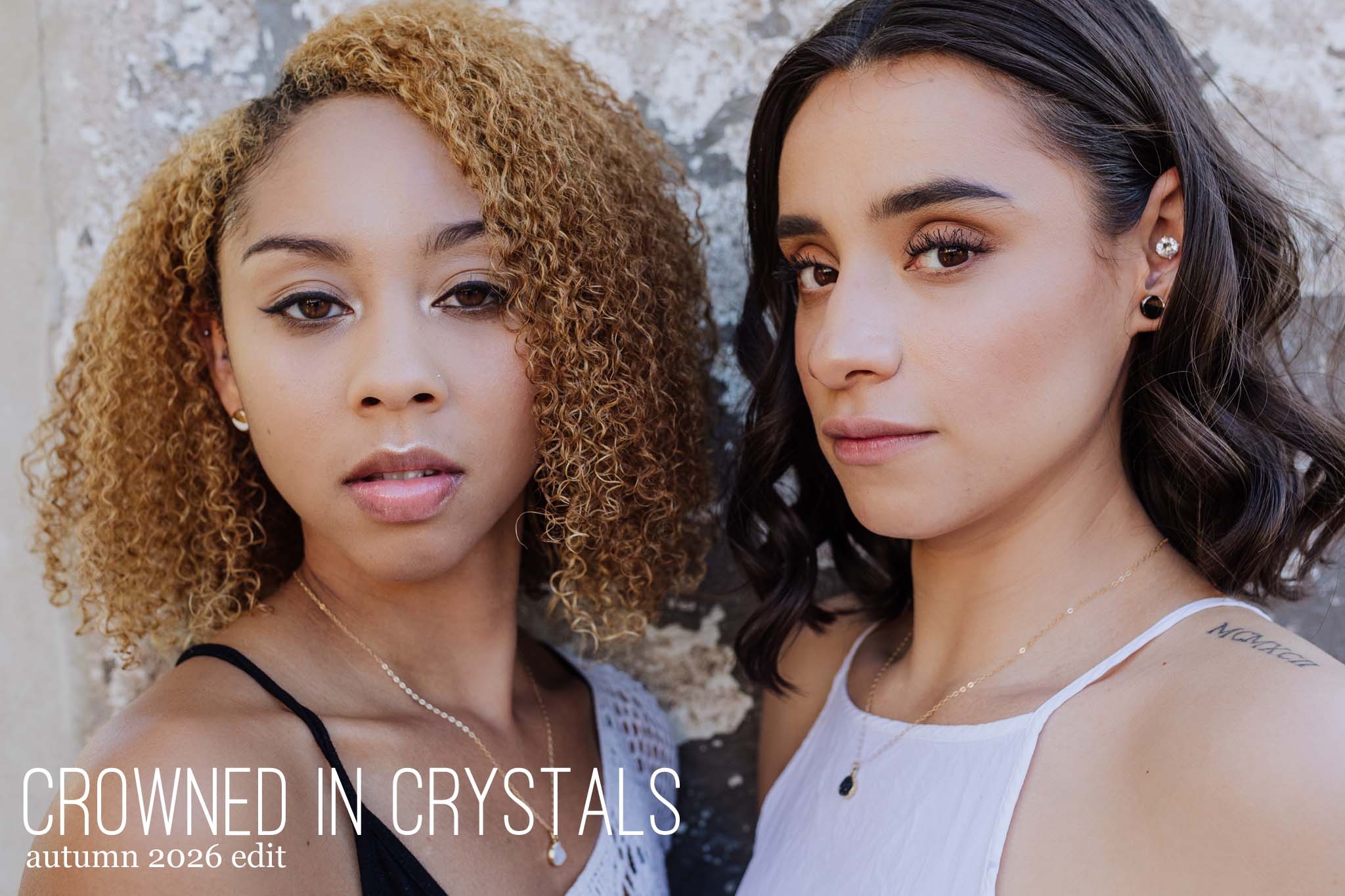 Two women wearing casual white clothing, modeling crystal jewelry.